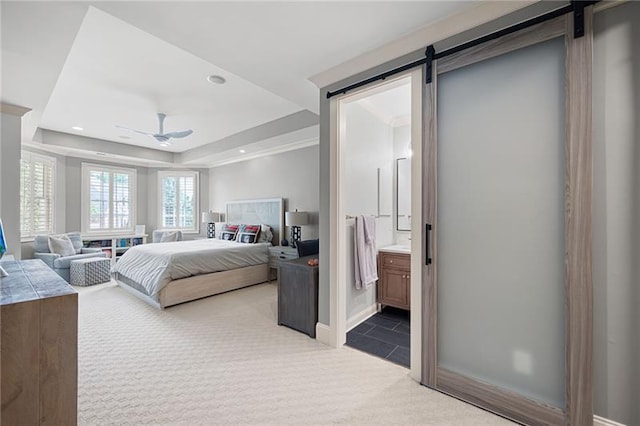 carpeted bedroom with ensuite bathroom, ceiling fan, a tray ceiling, and a barn door