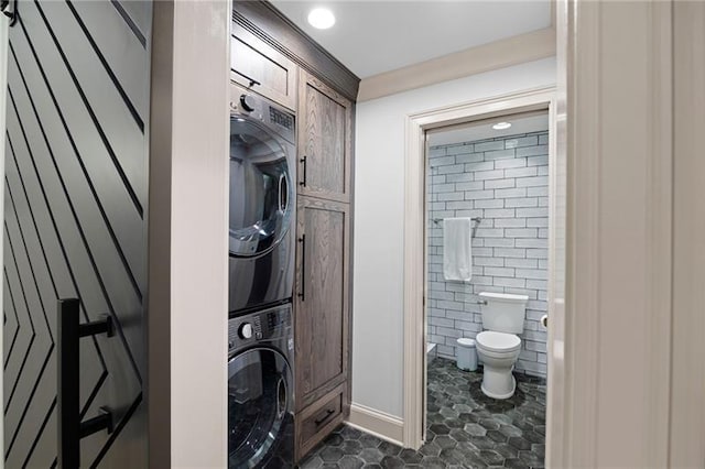 bathroom featuring toilet and stacked washer / dryer