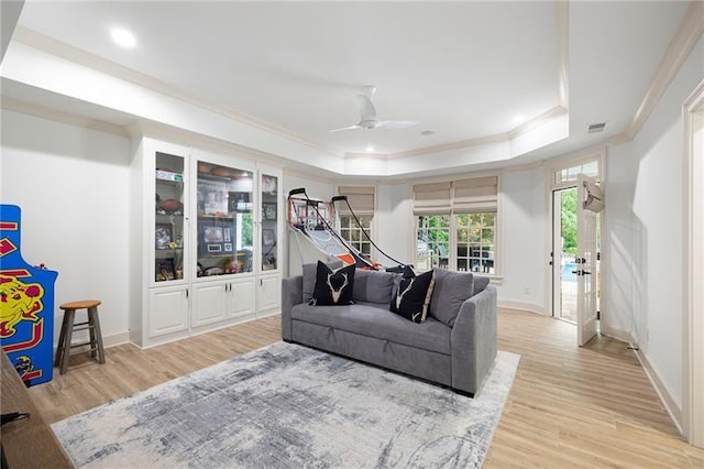 living room with a raised ceiling, ceiling fan, light hardwood / wood-style floors, and crown molding