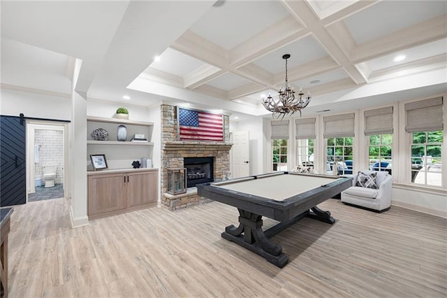 recreation room featuring an inviting chandelier, pool table, light hardwood / wood-style floors, a barn door, and a stone fireplace