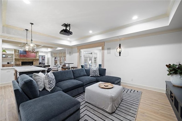 living room with light hardwood / wood-style floors, ornamental molding, a fireplace, and a tray ceiling