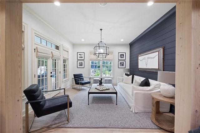 living room with light hardwood / wood-style floors, ornamental molding, french doors, wooden walls, and an inviting chandelier