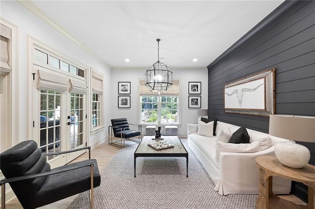 living room with wooden walls, an inviting chandelier, french doors, light hardwood / wood-style flooring, and crown molding