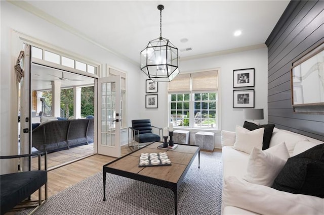 living room with french doors, wooden walls, light wood-type flooring, an inviting chandelier, and ornamental molding