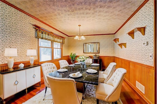 dining space featuring hardwood / wood-style flooring, ornamental molding, a chandelier, and a textured ceiling