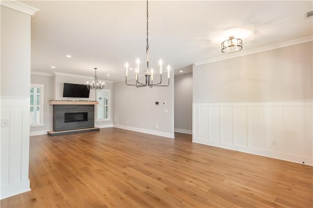 unfurnished living room with visible vents, a glass covered fireplace, a decorative wall, a chandelier, and light wood finished floors