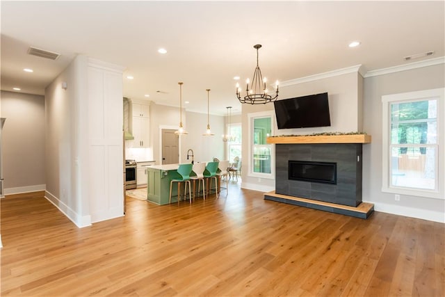living area with an inviting chandelier, baseboards, a healthy amount of sunlight, light wood-type flooring, and visible vents