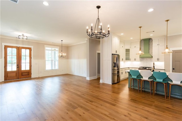 interior space featuring wall chimney range hood, wood finished floors, a chandelier, stainless steel fridge, and ornamental molding