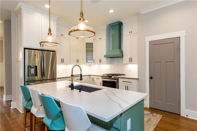 kitchen featuring wall chimney range hood, appliances with stainless steel finishes, a sink, dark wood finished floors, and backsplash