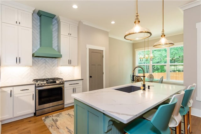 kitchen with gas stove, wall chimney range hood, light wood finished floors, and a sink