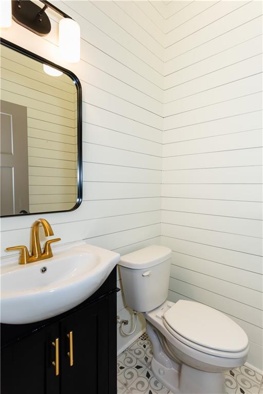 bathroom featuring vanity, wood walls, and toilet