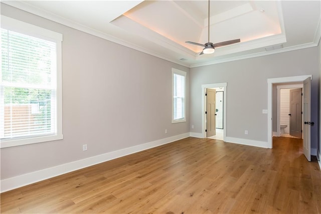 spare room with visible vents, crown molding, a tray ceiling, a ceiling fan, and light wood-style flooring