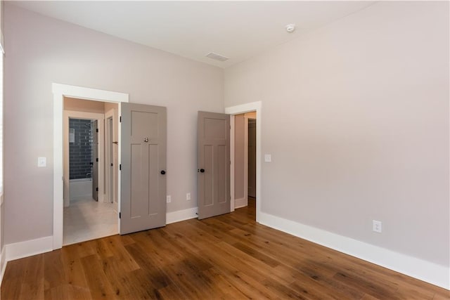 unfurnished bedroom featuring baseboards, wood finished floors, and visible vents