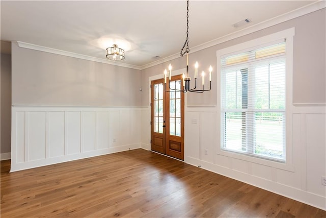 unfurnished dining area featuring an inviting chandelier, wainscoting, a decorative wall, wood finished floors, and ornamental molding