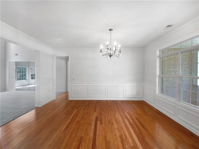 empty room with hardwood / wood-style flooring, crown molding, an inviting chandelier, and plenty of natural light