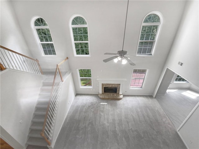 unfurnished living room featuring ceiling fan, carpet flooring, a fireplace, and a high ceiling