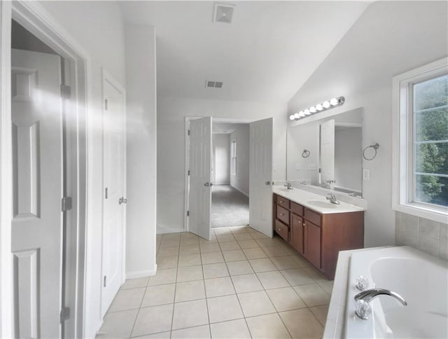 bathroom with a tub to relax in, vaulted ceiling, vanity, and tile patterned floors