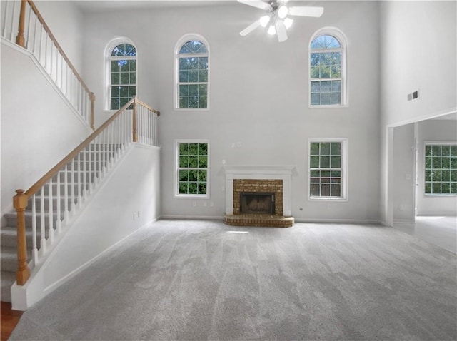 unfurnished living room with a high ceiling, ceiling fan, a fireplace, and carpet flooring