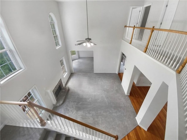 interior space with a brick fireplace, a towering ceiling, ceiling fan, and hardwood / wood-style floors