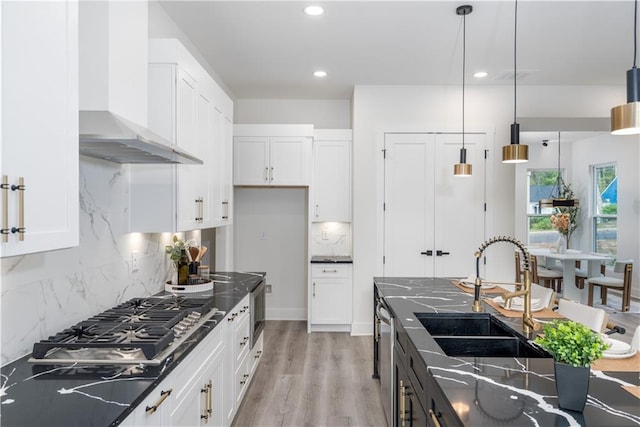 kitchen featuring wall chimney exhaust hood, pendant lighting, decorative backsplash, white cabinets, and sink