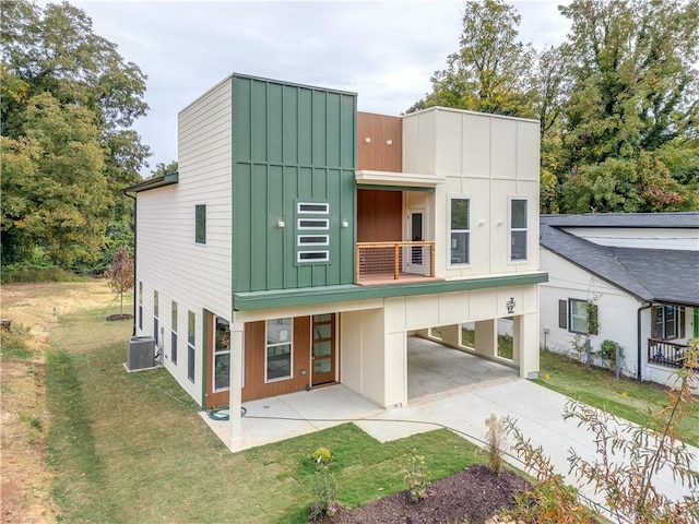 back of property with a lawn, a carport, a balcony, and central AC unit