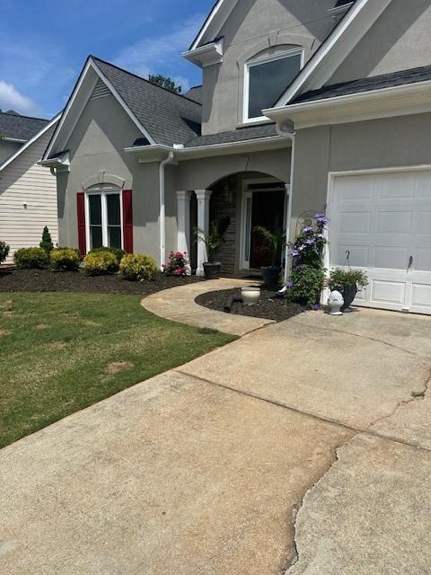 280 Ridge Bluff Ln, Suwanee, GA 30024 - doorway to property featuring stucco siding, a yard, concrete driveway, and a shingled roof