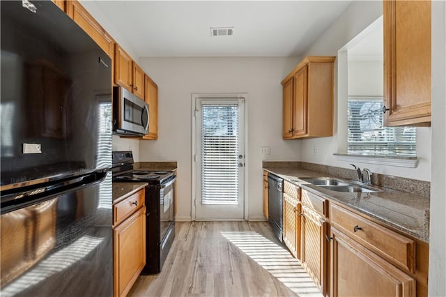 kitchen with sink, black appliances, dark stone counters, and light hardwood / wood-style flooring