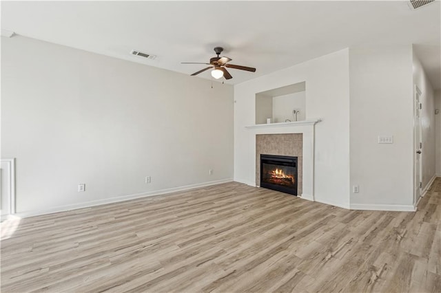 unfurnished living room featuring ceiling fan, a tiled fireplace, and light hardwood / wood-style floors