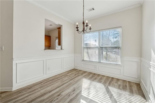 unfurnished dining area featuring crown molding, a notable chandelier, and light wood-type flooring