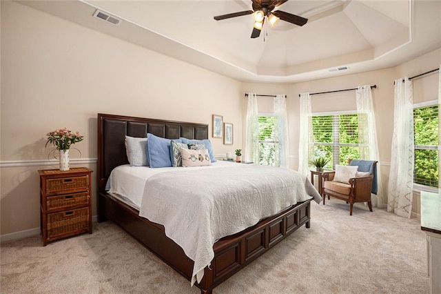 bedroom with light colored carpet, a ceiling fan, and a tray ceiling