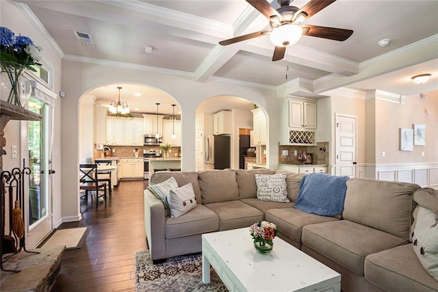living area with arched walkways, dark wood-style floors, ornamental molding, a ceiling fan, and a chandelier