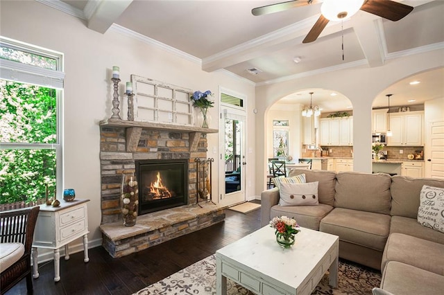 living room featuring crown molding, dark wood finished floors, arched walkways, a fireplace, and ceiling fan