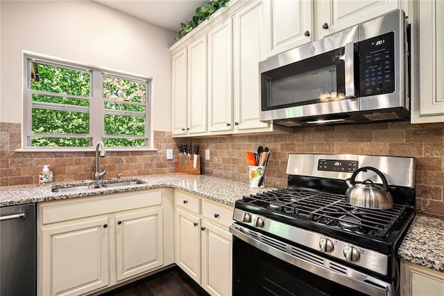 kitchen with stainless steel appliances, a sink, tasteful backsplash, and light stone countertops