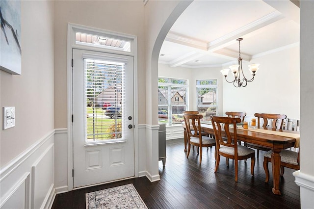 entrance foyer with beamed ceiling, ornamental molding, dark wood-style floors, arched walkways, and a decorative wall