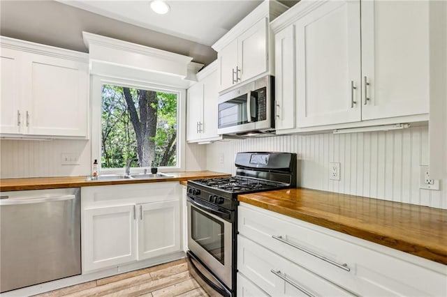 kitchen with white cabinets, stainless steel appliances, a sink, wood counters, and light wood-style flooring