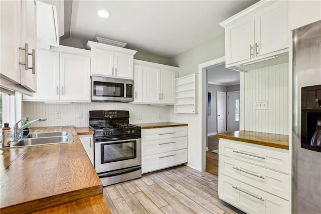 kitchen featuring white cabinets, stainless steel appliances, a sink, wood counters, and light wood-style flooring