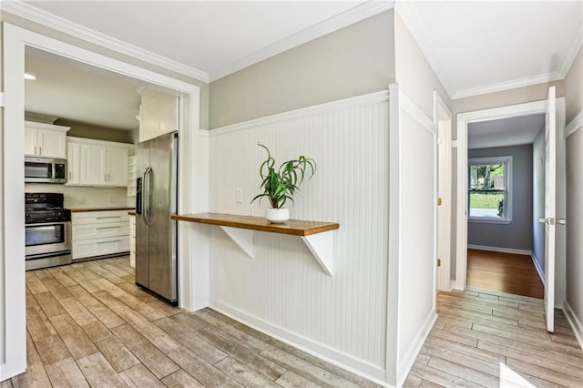 kitchen featuring a wainscoted wall, stainless steel appliances, ornamental molding, light wood-style floors, and white cabinetry