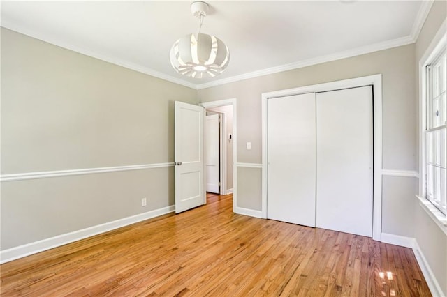 unfurnished bedroom with a closet, light wood-type flooring, an inviting chandelier, baseboards, and ornamental molding
