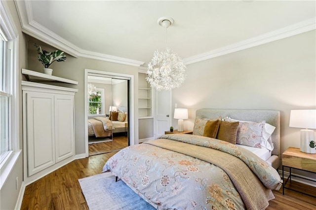 bedroom with wood finished floors, ornamental molding, a closet, baseboards, and a notable chandelier