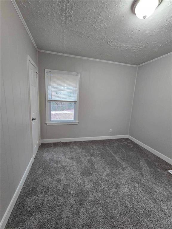 unfurnished room with dark carpet, crown molding, and a textured ceiling