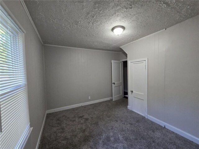 spare room featuring crown molding, a textured ceiling, and dark colored carpet