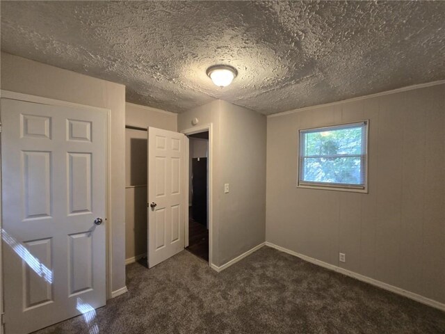 unfurnished bedroom with baseboards, dark colored carpet, and a textured ceiling