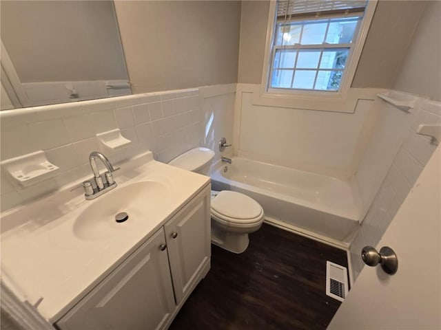 full bathroom with vanity, a tub to relax in, visible vents, a wainscoted wall, and toilet