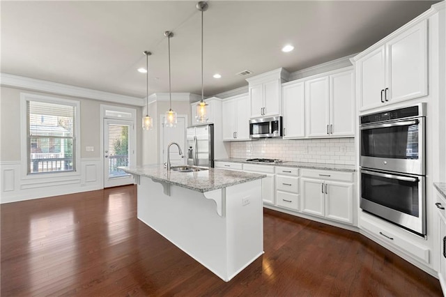 kitchen with white cabinets, hanging light fixtures, light stone countertops, an island with sink, and appliances with stainless steel finishes