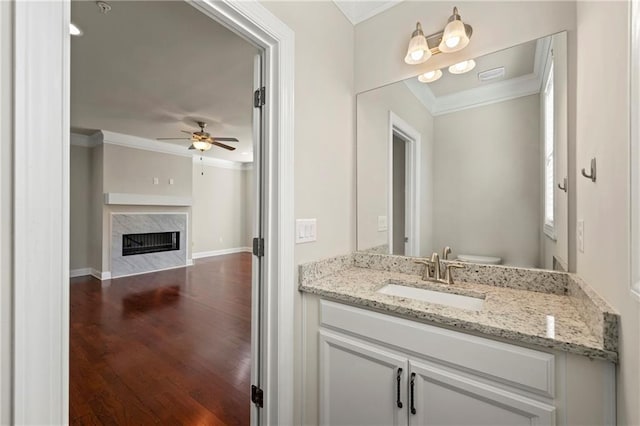 bathroom with ceiling fan, crown molding, wood-type flooring, a fireplace, and vanity