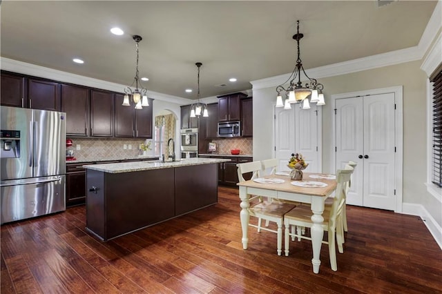 kitchen with dark wood-type flooring, a kitchen island with sink, decorative light fixtures, and appliances with stainless steel finishes