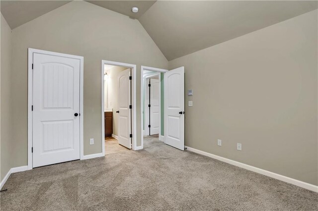 unfurnished bedroom with ensuite bathroom, light colored carpet, and vaulted ceiling