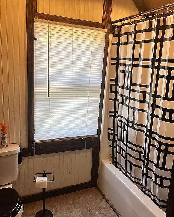 bathroom featuring toilet, shower / bath combo, and wooden walls