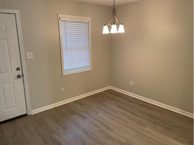 spare room with an inviting chandelier and dark hardwood / wood-style flooring