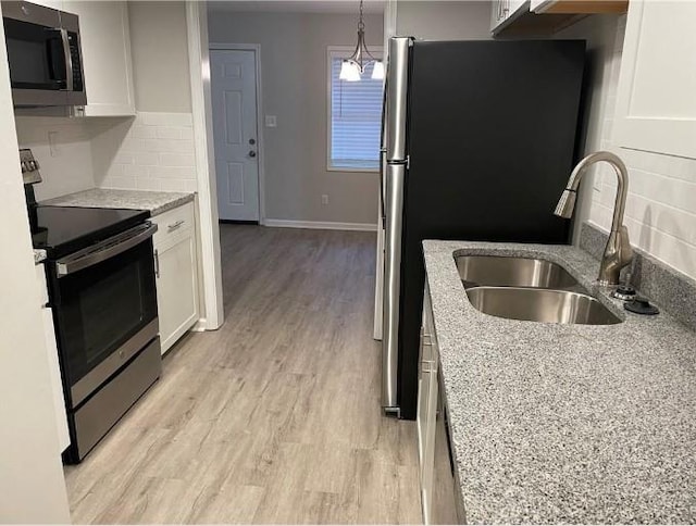 kitchen with white cabinetry, light hardwood / wood-style flooring, appliances with stainless steel finishes, light stone counters, and tasteful backsplash